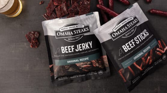 One package of Omaha Steaks beef jerky and one package of Omaha Steaks beef sticks open with several pieces of jerky poking out from the bags.