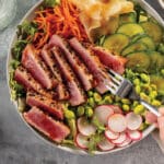 Yellowfin tuna sushi salad bowl with greens, cartots, cucumbers, edamame, radishes and ginger with sliced medium-rare tuna.