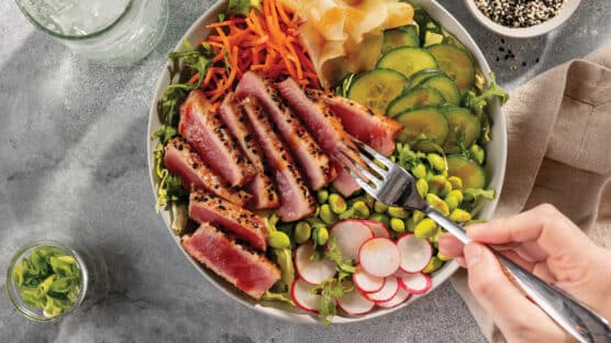 Yellowfin tuna sushi salad bowl with greens, cartots, cucumbers, edamame, radishes and ginger with sliced medium-rare tuna.