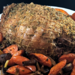 herbed boneless leg of lamb roast with purple and oranges carrots on white plate