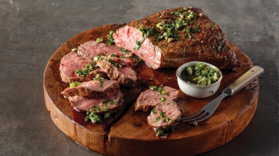 Tri-tri roast partially cut into slices and cooked medium rare with chimichurri sauce drizzled over it.
