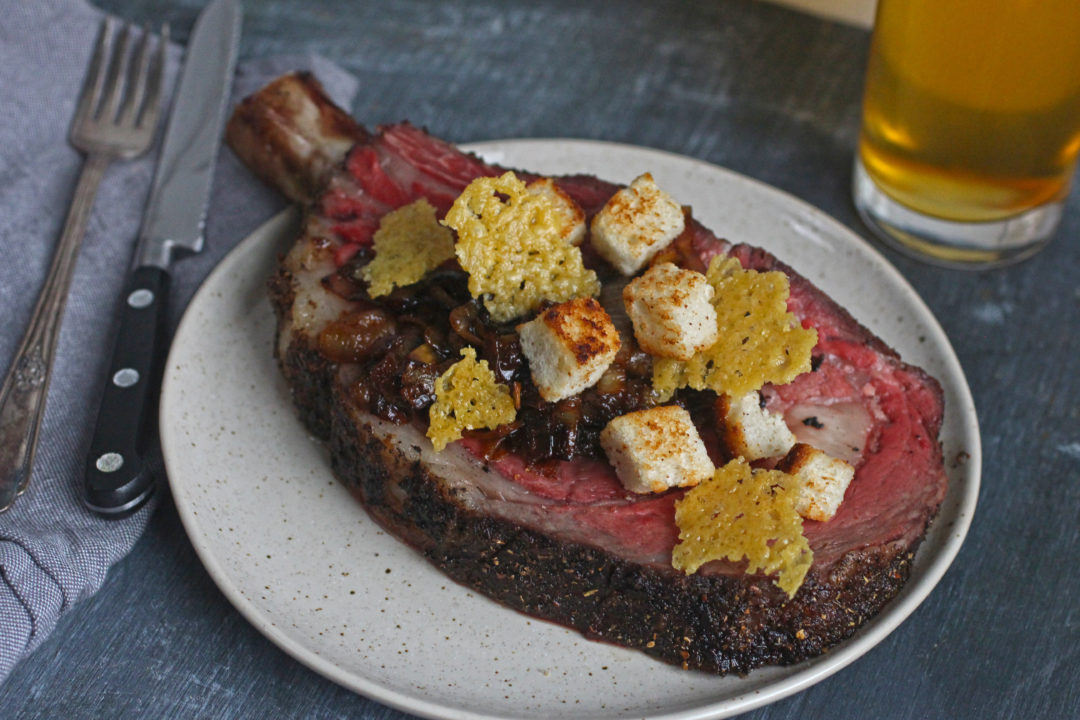 Plated prime rib slice cooked medium rare topped with croutons, onions and cheese
