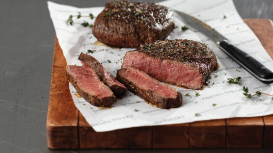 Cutting board with two cooked flat iron steaks, one sliced open and cooked medium-rare.