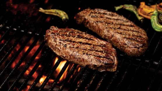 Two New York strip steaks on lit grill with perfect grill marks.