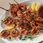 Grilled shrimp on skewers plated with cocktail sauce and lemon wedges