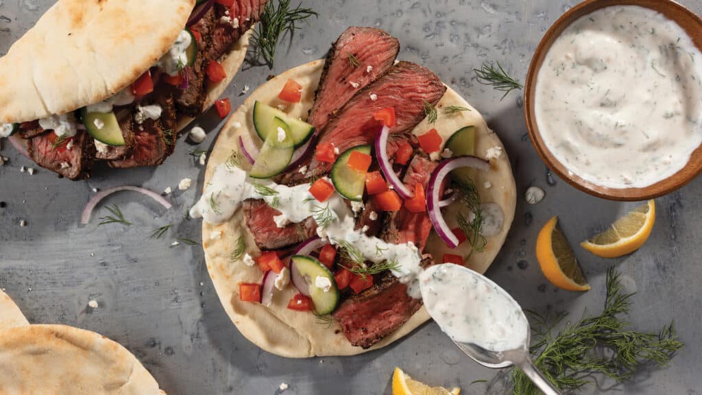 Gyros with medium-rare sliced top sirloin steak, fresh cucumbers, sliced red onions with drizzled tzatziki sauce