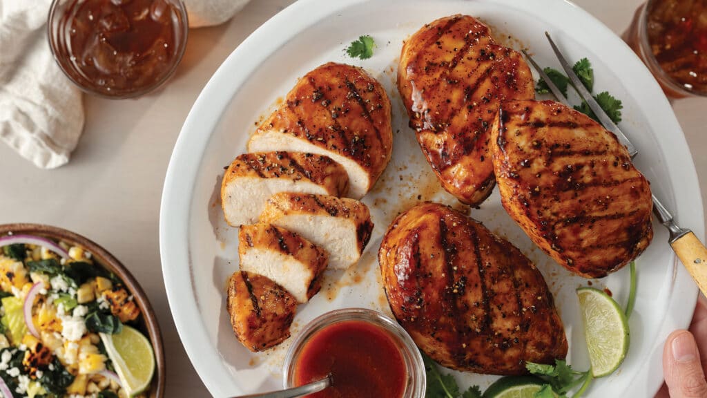 Four barbecue marinated chicken breast on a white plate served with BBQ sauce