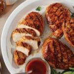 Four barbecue marinated chicken breast on a white plate served with BBQ sauce