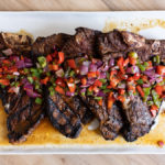 Four ancho chili rubbed porterhouse steaks with grilled onion and pepper salsa on a plate