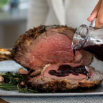 Pouring red wine sauce over sliced prime rib