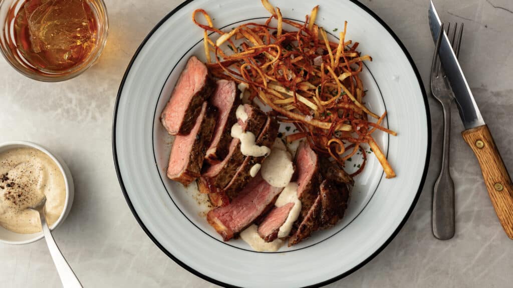 Strip steak cooked medium rare and cut into 1/2 thick slices served with steak au poivre sauce and crispy fries.
