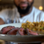 Chef David holding plate of sweet soy top sirloin, quinoa fried rice and cauliflower puree