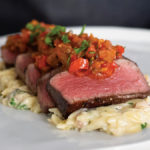 Reverse seared, medium-rare sliced filet mignon served with creamy orzo pasta with pancetta and topped with caponata