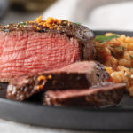 Suya-Dusted filet mignon sliced and cooked to medium-rare served with "red rice" risotto on a gray plate