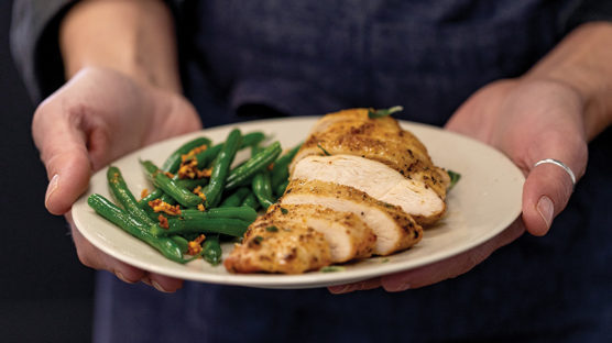 Woman holding white plate with sliced air fried chicken breast and green beans with bacon