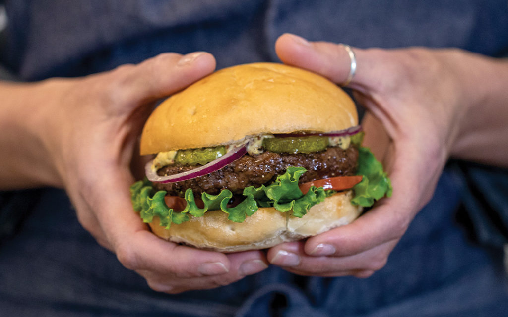 Person who holding hamburger with air fried burger, lettuce, tomato, pickles and red onion