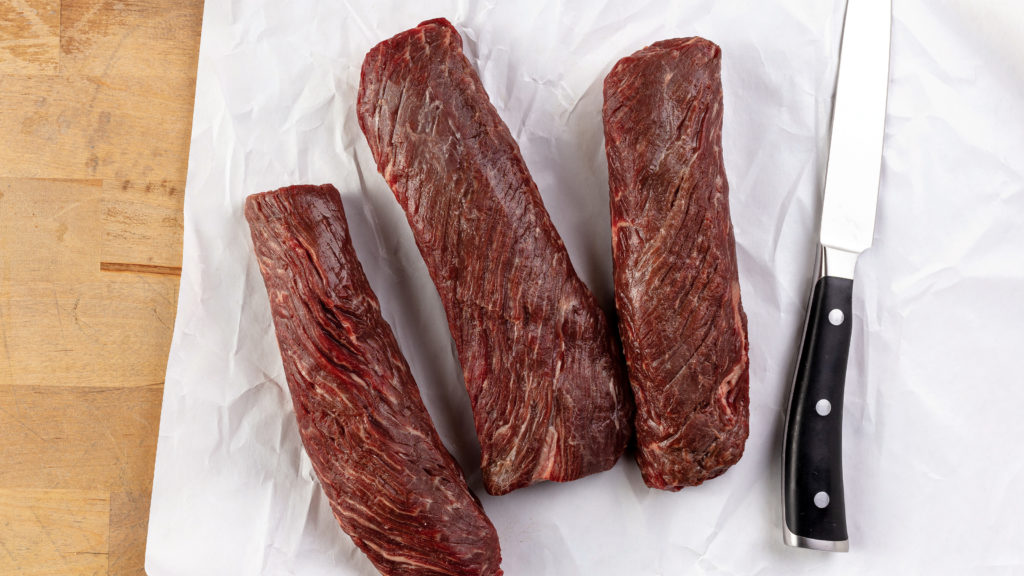 Three raw hanger steaks and a knife on butcher's paper