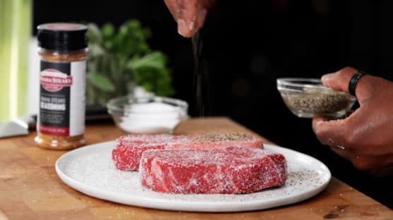chef seasoning two steaks with salt and pepper
