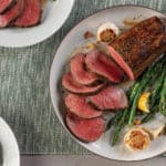 Roasted whole chateaubriand cooked medium-rare and sliced served with lemon-garlic asparagus on white plate