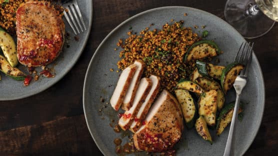 Sliced, boneless hot honey pork chop served with paprika-dusted zucchini served on grey plate.