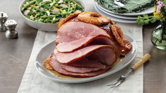 Sliced Duroc ham with pineapple slices plated on table next to dish of green beans.