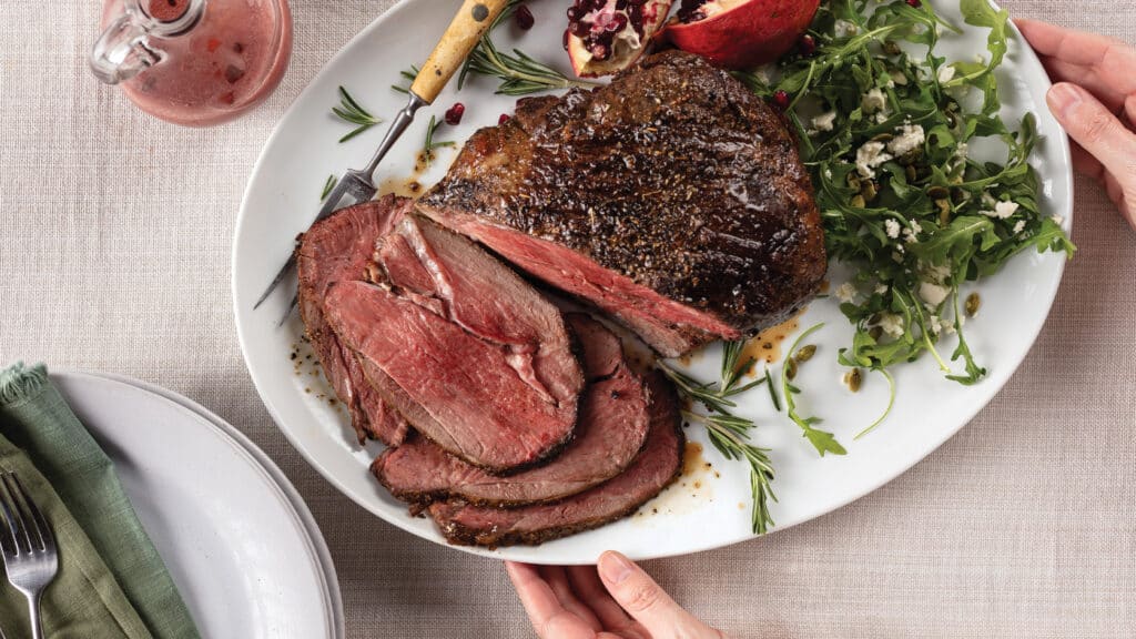 Coriander-Crusted Leg of Lamb with Arugula and Feta Salad with Pomegranate Vinaigrette on white platter