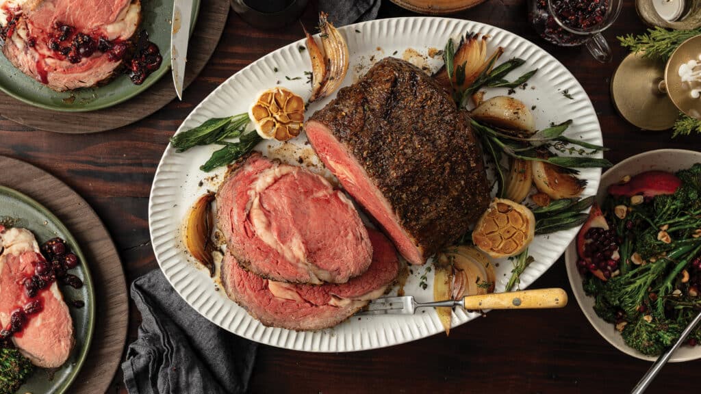 Holiday table setting with prime rib roast cooked medium rare sliced on a white platter garnished with lemon.