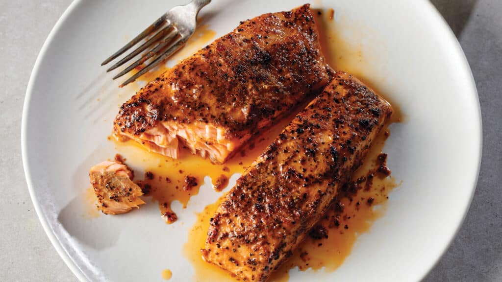 Two cooked salmon fillets on white plate with fork