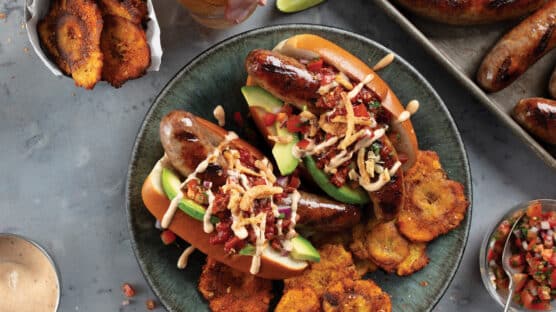 Two juicy hot dogs piled high with chorizo chili, fresh pico de gallo, creamy avocado, chipotle aioli, and crispy shallots and served with bbq tostones.