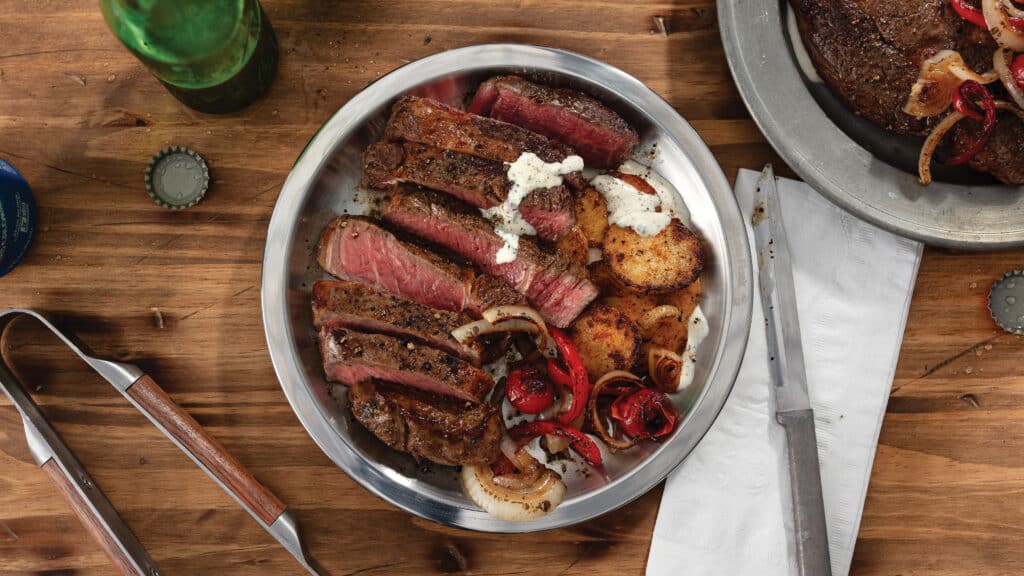 Pan-seared medium-rare ribeye sliced with drizzle of whipped cotija cheese sauce and served with crispy potatoes and cherry tomato saute