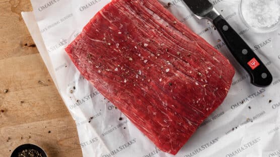Uncooked flank steak on Omaha Steaks butcher's paper next to knife