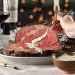 Holiday table with medium-rare prime rib roast sliced with person adding a dollop of jalapeno crema.