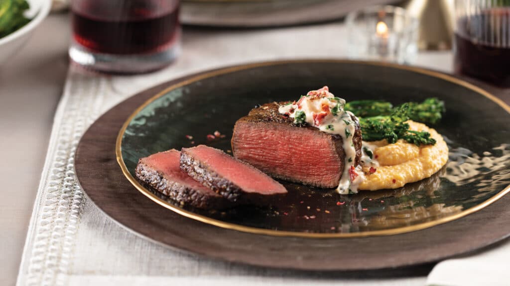 Sliced filet mignon with creamy-lobster spinach sauce with cheddar grits on a brown ceramic plate