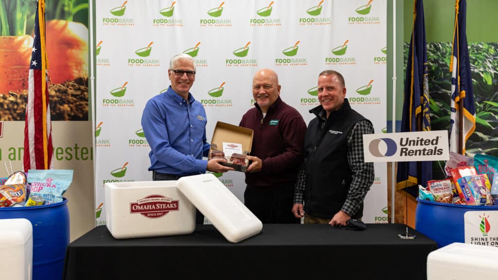 representatives from Omaha Steaks, Food Bank for the Heartland and United Rentals holding a box of Omaha Steaks