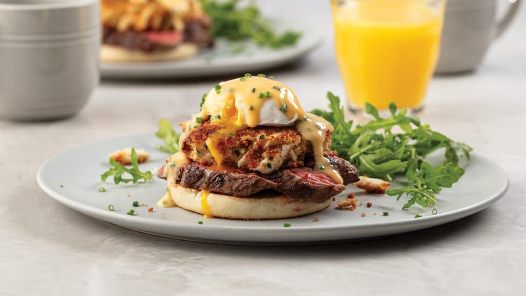 Steak crab cake Benedict on a white plate and served with orange juice