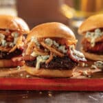 3 Bacon black 'n blue cheese sliders with crispy onion straws on a platter.