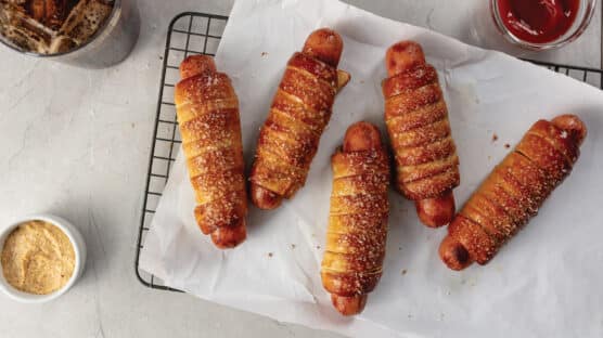 5 cooked gourmet pretzel hot dogs cooling on a parchment paper-lined wire rack.