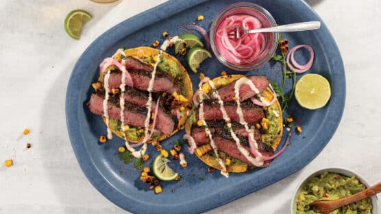 Two Grilled Flat Iron Steak Tostadas with Coconut-Chili Mayo and Guacamole served with pickled onions on a blue plate