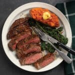 White plate with sliced medium-rare pan-seared ribeye, roasted broccoli and sweet potato.