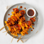 BBQ chicken and pineapple skewers on a grey plate with a side of BBQ sauce