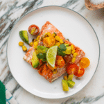 White plate with grilled salmon topped with fresh salsa