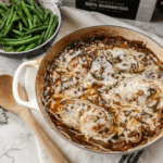 French onion chicken in a white skillet on counter next to a dish of green beans