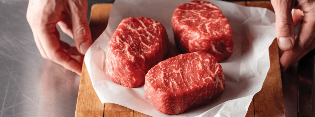 Three raw ribeye steaks on a cutting board.