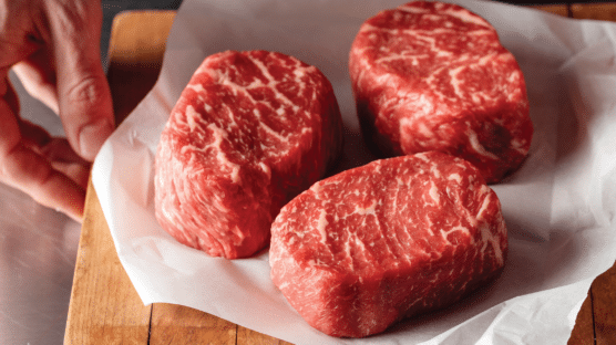 Three raw ribeye steaks on a cutting board.