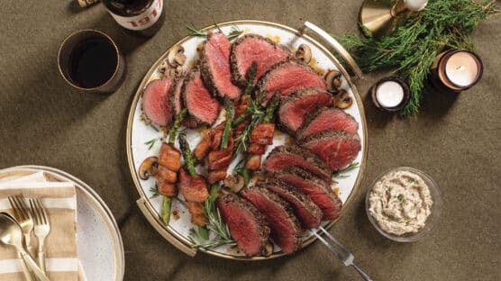 Duxelles-roasted chateaubriand cooked medium-rare, sliced and fanned out on plate with bacon-wrapped asparagus.