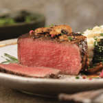 Filet Mignon cooked medium-rare with mushroom sauce served with garlic mashed potatoes and broccolini on a white plate.