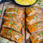 Eight orange-glazed Columbia King Salmon Fillets on wood planks next to a skillet of creamed corn.