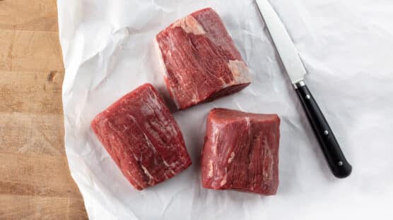 Three raw bistro steaks on butcher's paper next to a knife.