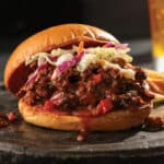 BBQ sloppy joe and chips on a silver plate served with a beer.