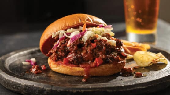 BBQ sloppy joe and chips on a silver plate served with a beer.